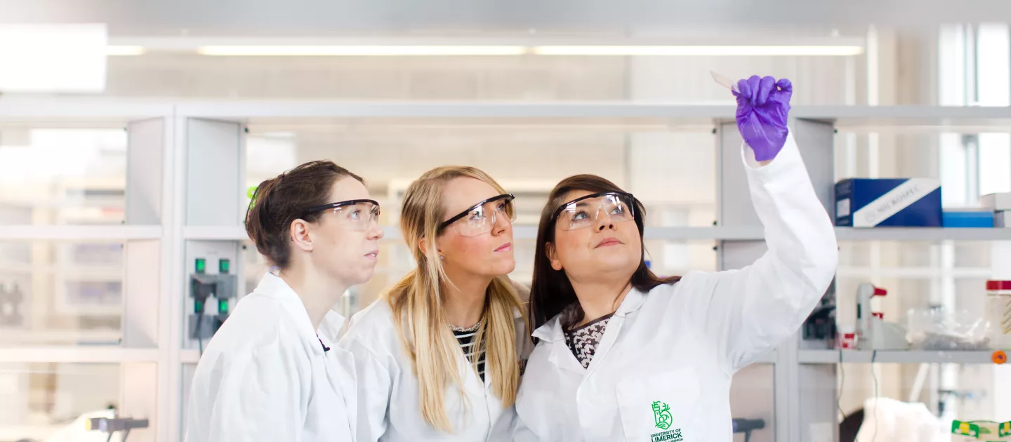 three women in lab coats examining test tube