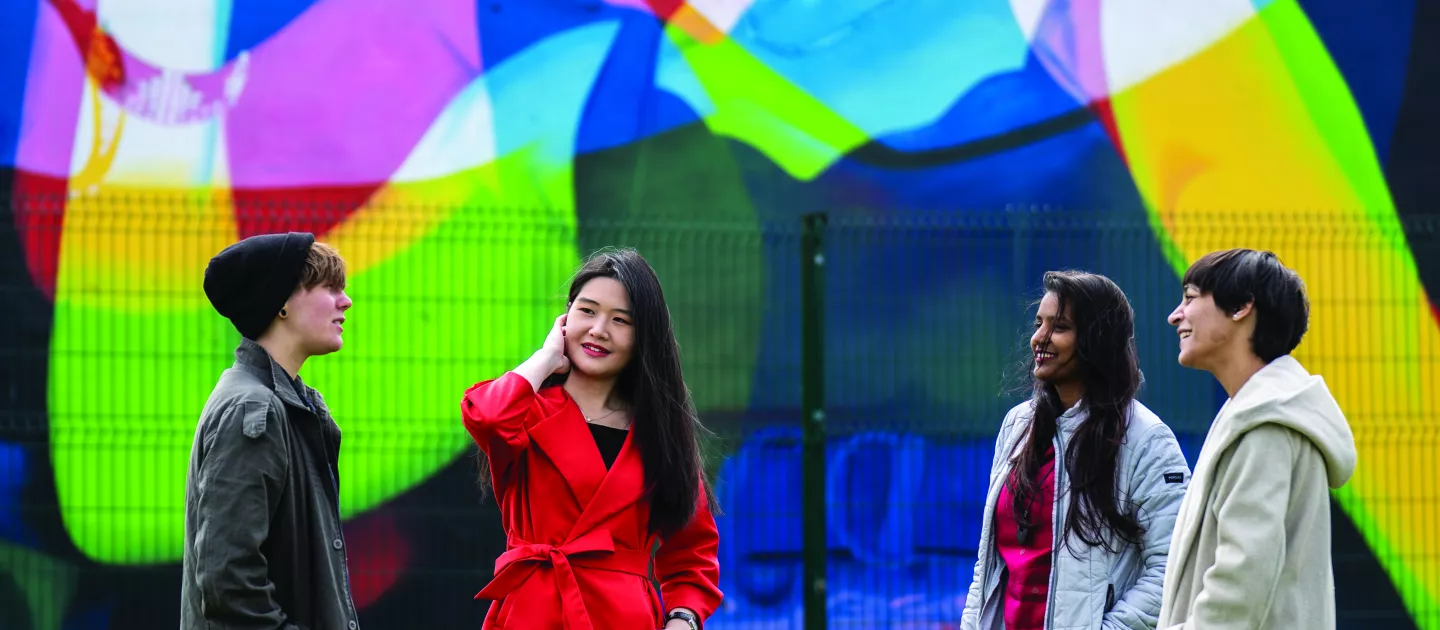 four students standing in front of wall mural