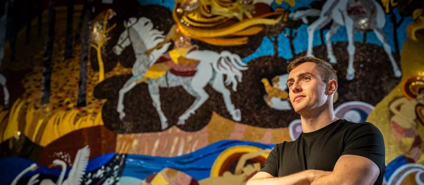 Joseph Mooney standing in front of mural in UL with his arms crossed