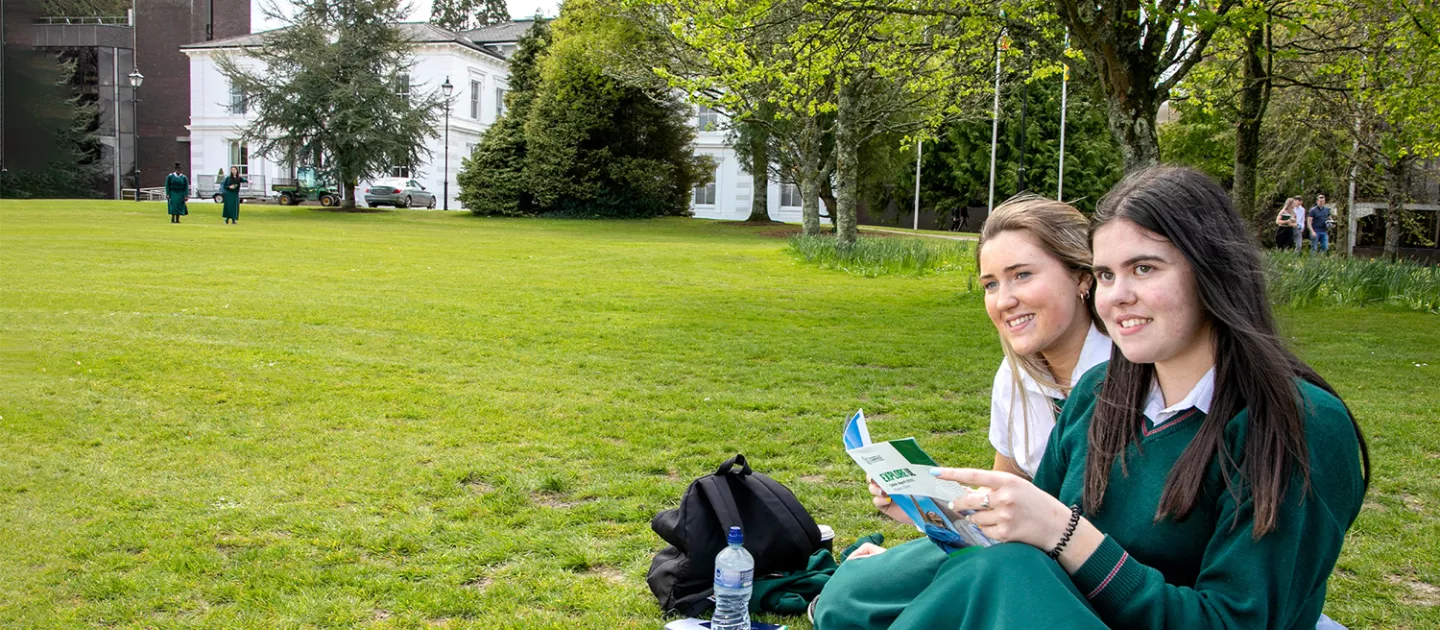 two female students sitting outside in a green area