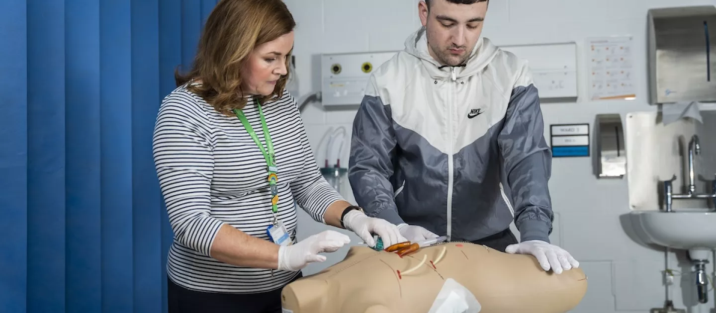 Photo of a student learning from a teacher on a medical dummy