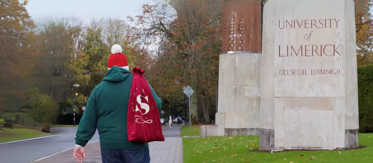 Person carrying a red sack walking near the University of Limerick sign.