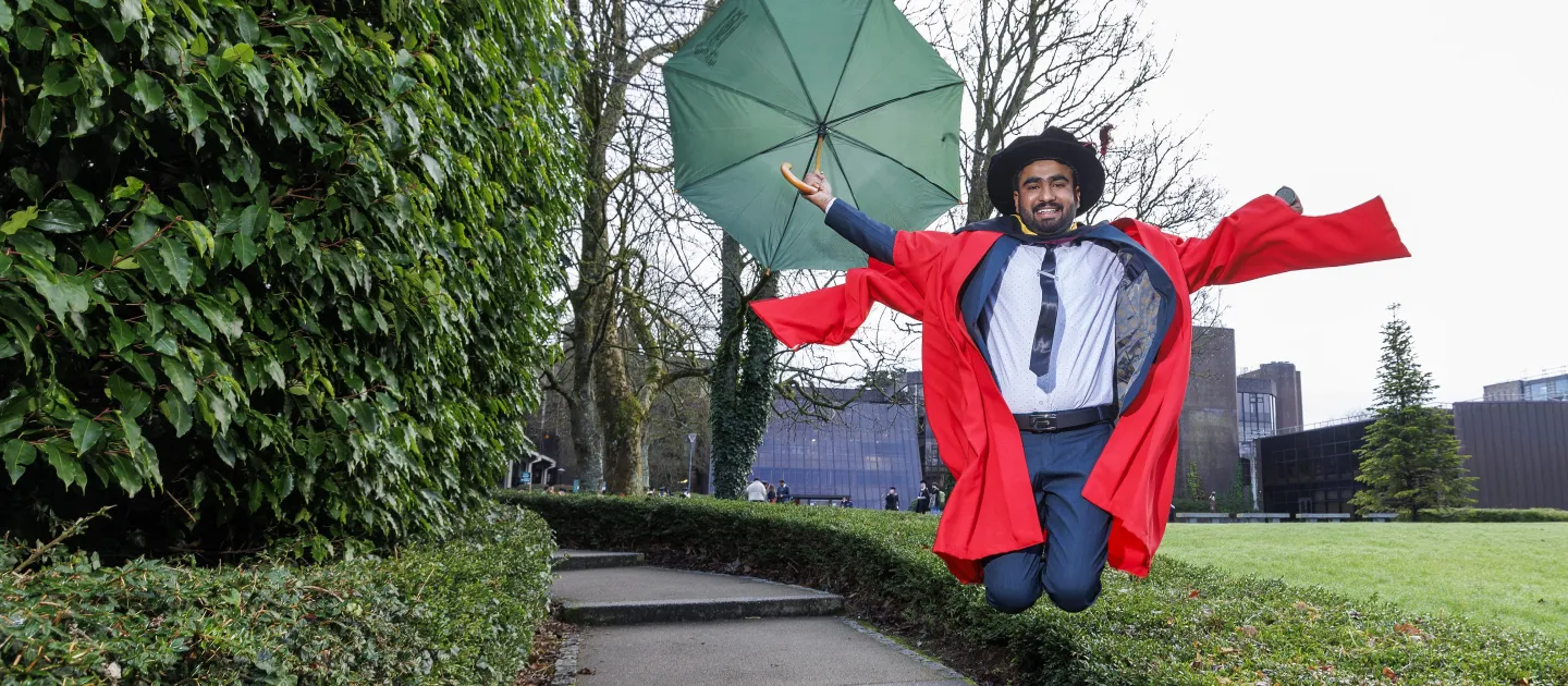 Muddasar holding a UL umbrella and jumping in his PhD robes