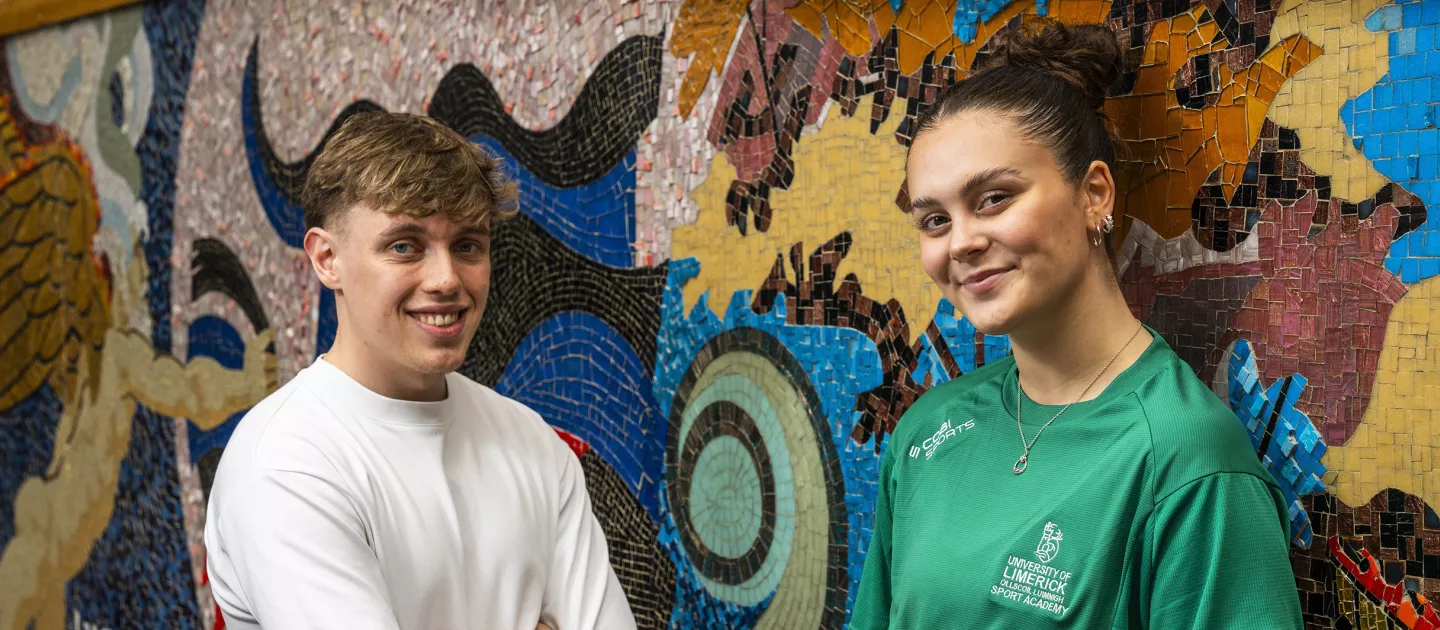 two students standing by a mosaic wall mural