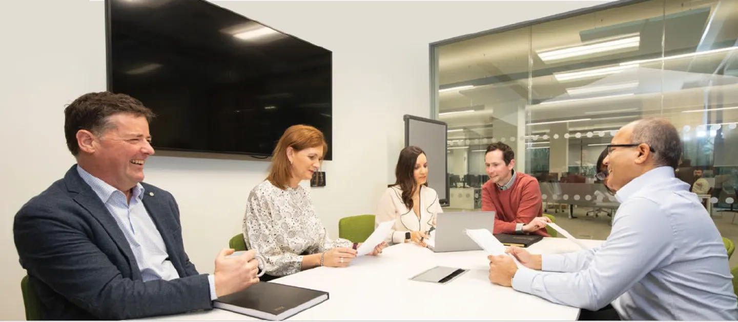 Image shows five people around a table chatting and laughing 