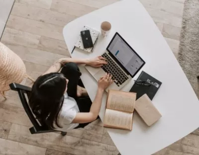 Aerial view of a lady typing on the keyboard of a laptop on a desk in a living room.