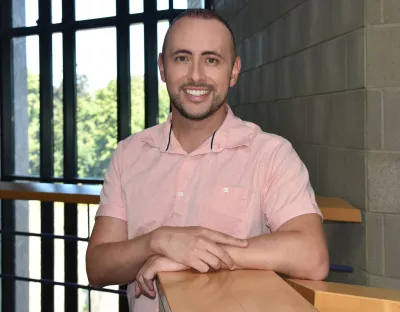 Dr Daniel Granato leaning on a wooden banister, wearing a salmon coloured shirt and smiling into the camera