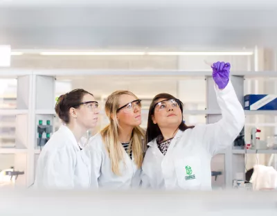 three women in lab coats examining test tube