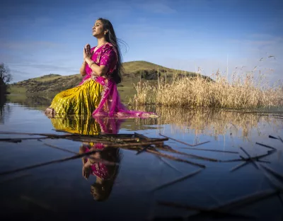 A woman sits in a lake wearing a traditional Telugu outfit consisting of a  pink voni and yellow lehenga, symbolising  happiness and prosperity. 