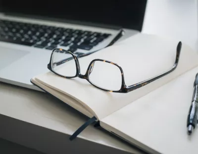 pair of glasses placed on top of an open book with a pen next to them