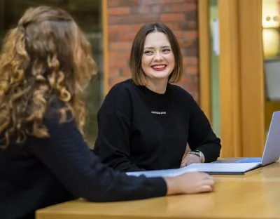 2 students chatting in library in front of laptop