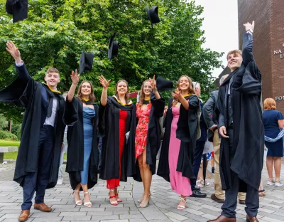 A group of students celebrate their graduation by throwing their hats in the air on the UL campus 