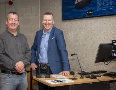 Two men standing near a desk facing the camera and smiling