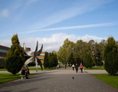 View from KBS of statue outside Schumann Building with people walking in front and trees in the background. 