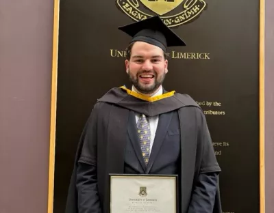 llm graduate doctor alex casey in his cap and gown holding his parchment at graduation