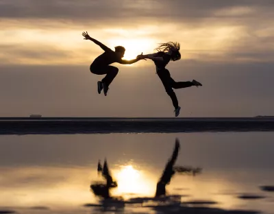 A photo of two dancers jumping against a beach background