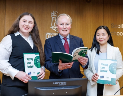 Two women and a man wearing suits smiling for a photo holding copies of the Plassey Law Review