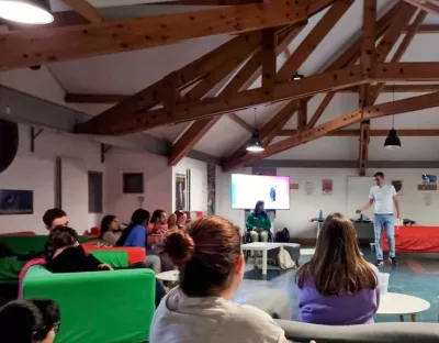 A student facilitator standing in the middle of a room leading a workshop, with student participants sat around the room listening and engaging