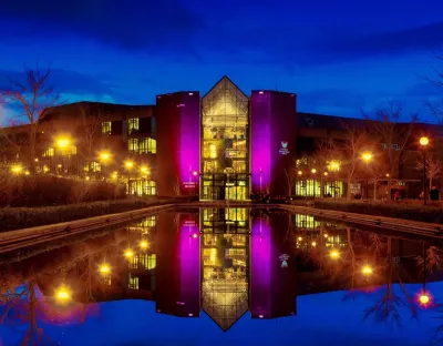 The exterior of the Foundation Building at University of Limerick, home to the University Concert Hall, lit up at night, with its image reflected in the fountain outside the Foundation Building