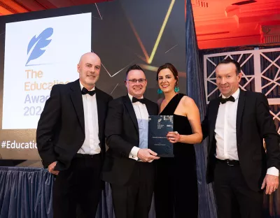 Three men and a woman in black tie clothing accepting an award on stage