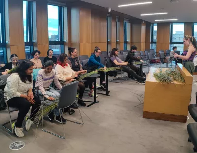 A photo of a group of students sat around a room understanding how to weave baskets with reeds