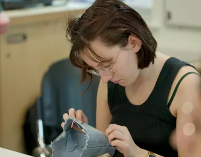 A photo of a student in UL's Makerspace learning how to mend clothes sustainably. The student is holding a piece of material and examining the repair work done.