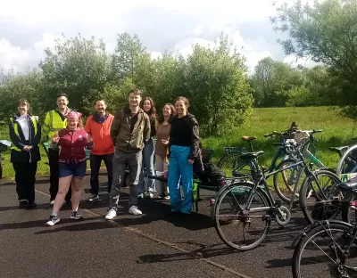 Group of students and staff stand next to bicycles with greenery in the background