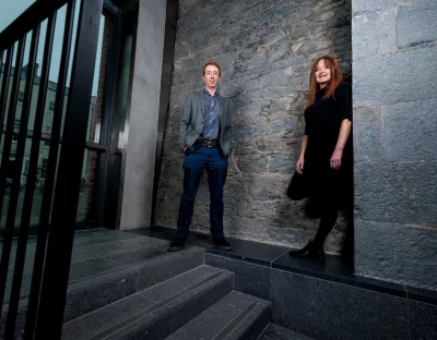 A photo of a male and female standing against a stone wall