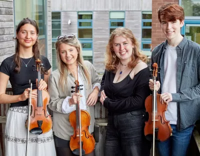 Four young adults holding violins smiling at the camera