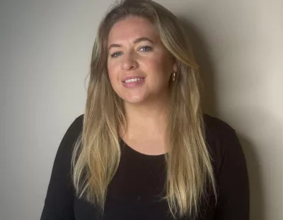 Blond haired woman in a black top standing in front of a black wall