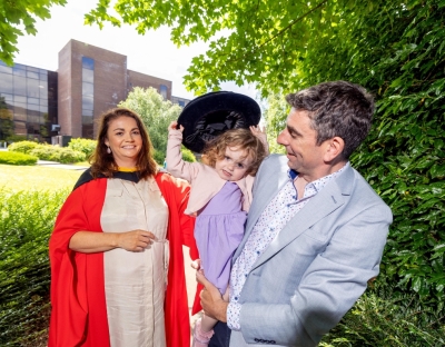 Graduate Audrey Galvin with family in front of UL Library. She wears PhD graduation gown which is red