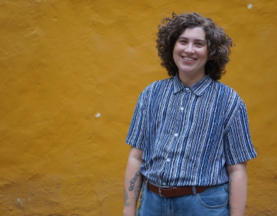 A person in a striped blue shirt and jeans standing in front of a yellow wall