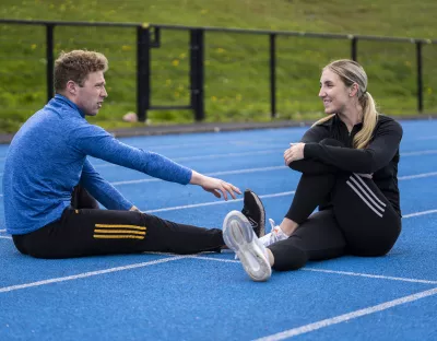 Man and woman sitting on UL athletics track stretching and warming up