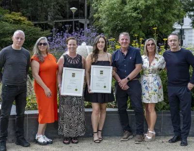 Three men and three women standing facing the camera with two women holding framed awards