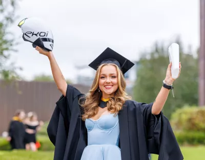 Woman graduating from university wearing a cap and gown and holding scroll and arrow helmet