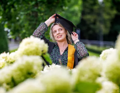 Picture of women wearing graduation robes with flowers out of focus in the foreground and trees in the background