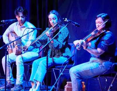 1 person playing a guitar and two people playing the fiddle