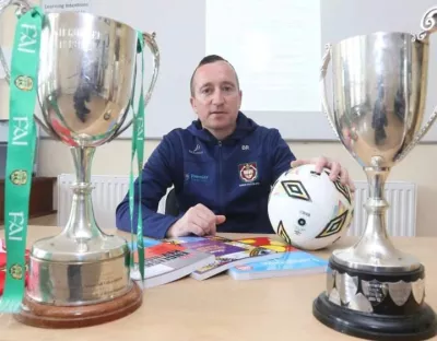 Man sitting behind desk with two football champion cups in front of him