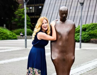 A blonde woman in a navy dress leaning on a brown statue