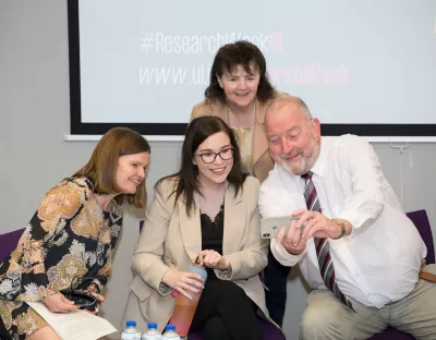 Image shows four people posing and smiling for a selfie