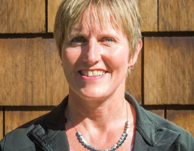 Photo of a woman with short blond hair standing against a wooden backdrop