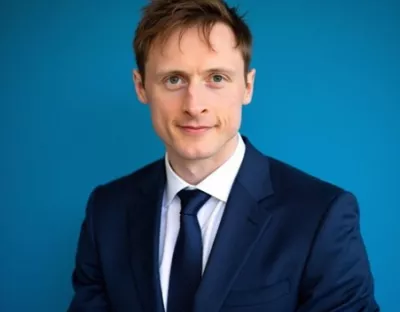 Fair haired man in navy suit with blue background