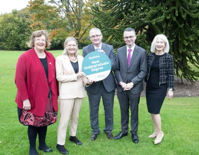 A group of five people at UL holding a sign that says new undergraduate degree. They are outside on the lawn of Plassey House at UL