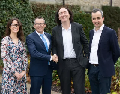 Four people are pictured together - the two men in the middle are shaking hands