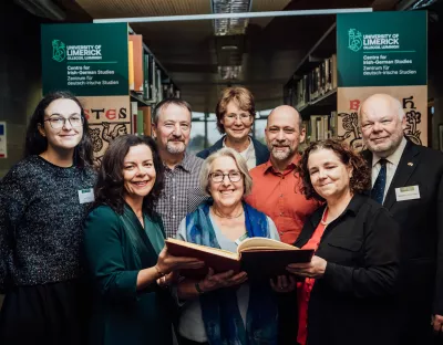 Group of people looking at large book in front of library shelves