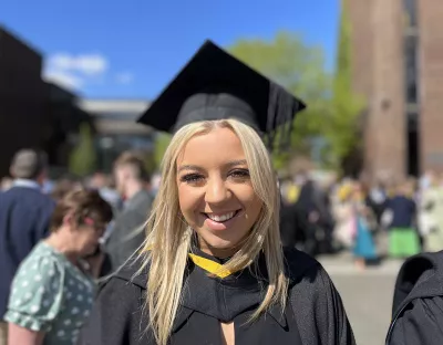 A woman with blonde hair wearing a black graduation cap and gown smiling at the camera