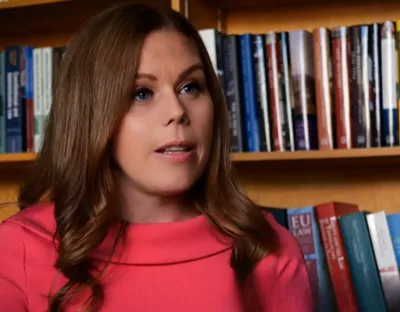 A photo of a woman speaking in front of a shelf of books