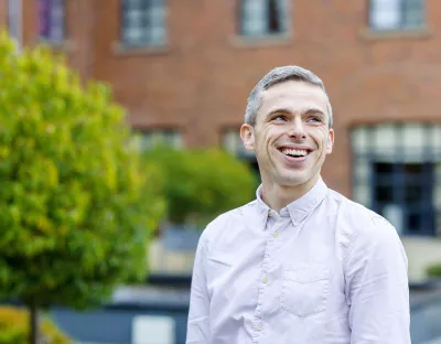 Smiling man standing outside in front of building and greenery 