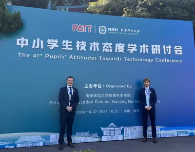 2 men in suits standing infront of a sign with Chinese writing