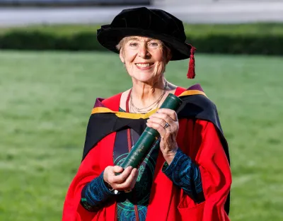 A photo of a woman in red graduation robes and black cap, holding a screen scroll in both hands